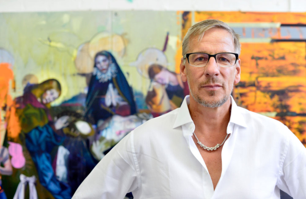 It shows the artist with his artwork in the background.
